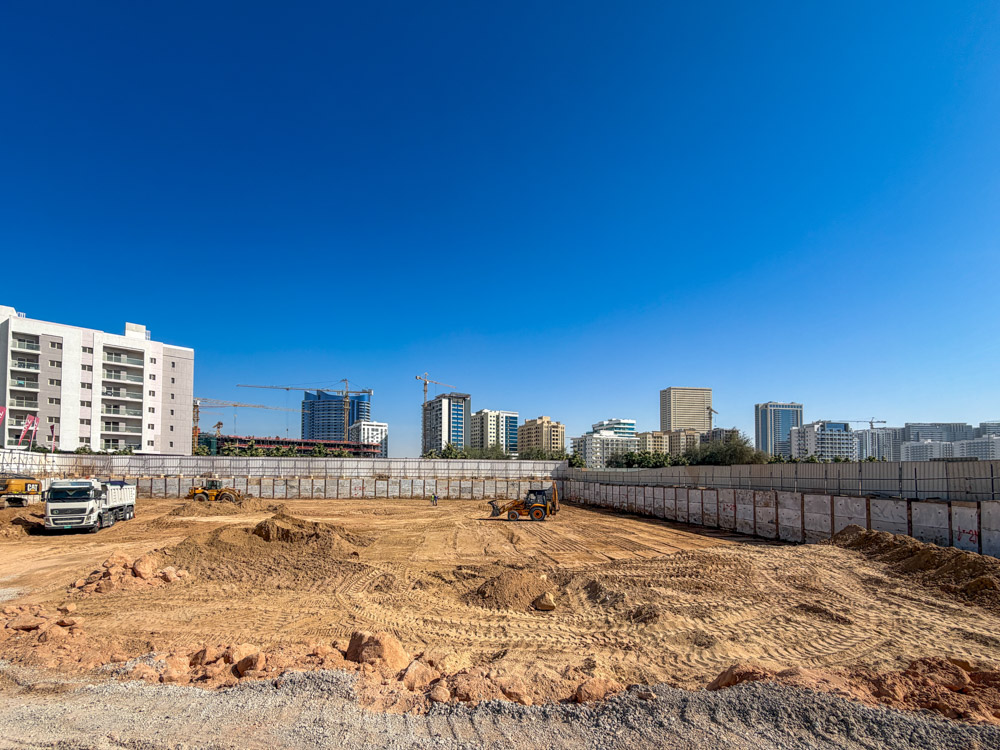 Cove Grand By Imtiaz Construction site with heavy machinery, surrounded by buildings under a clear blue sky. Ground is recently excavated.